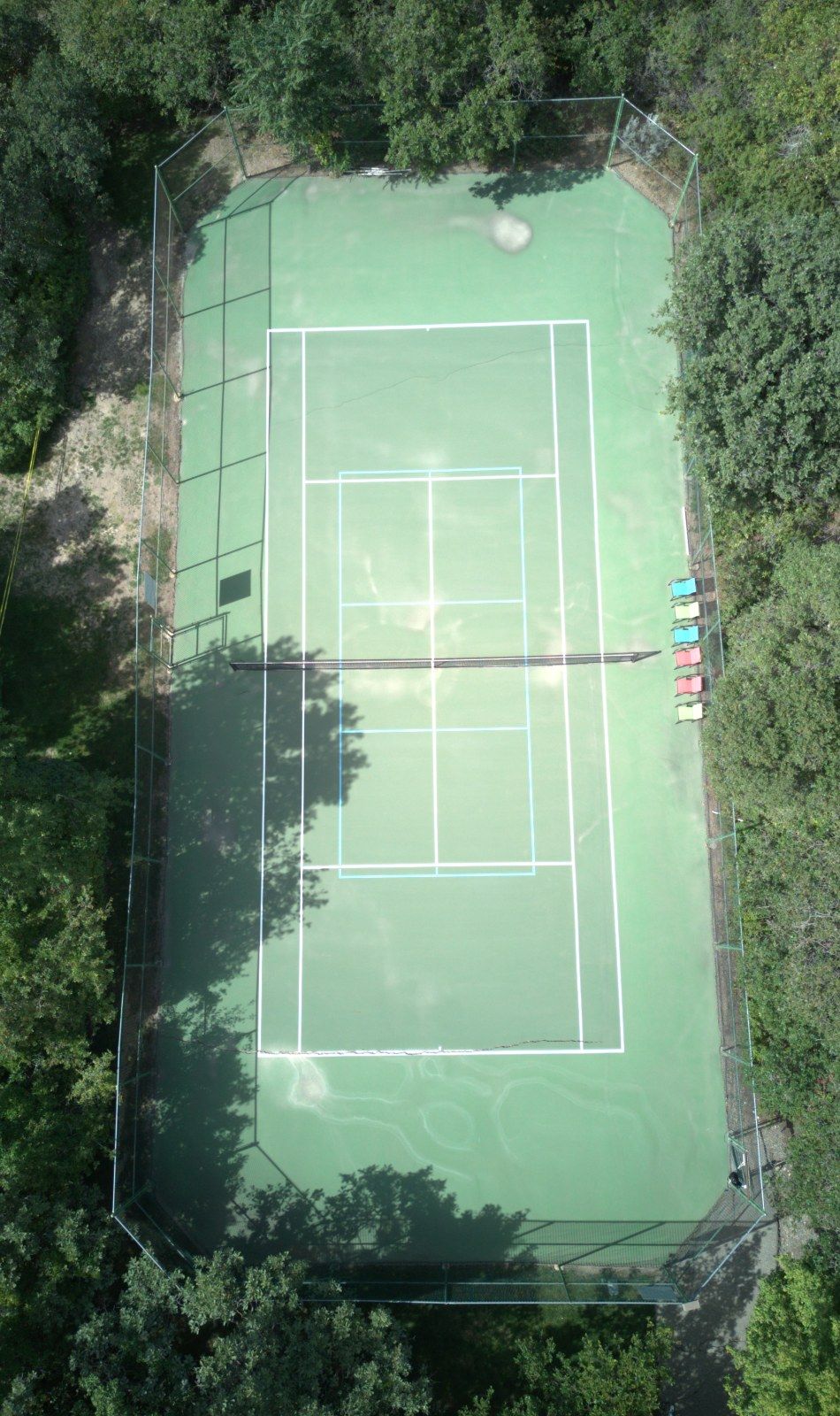 Worn, faded green tennis court before resurfacing, aerial view